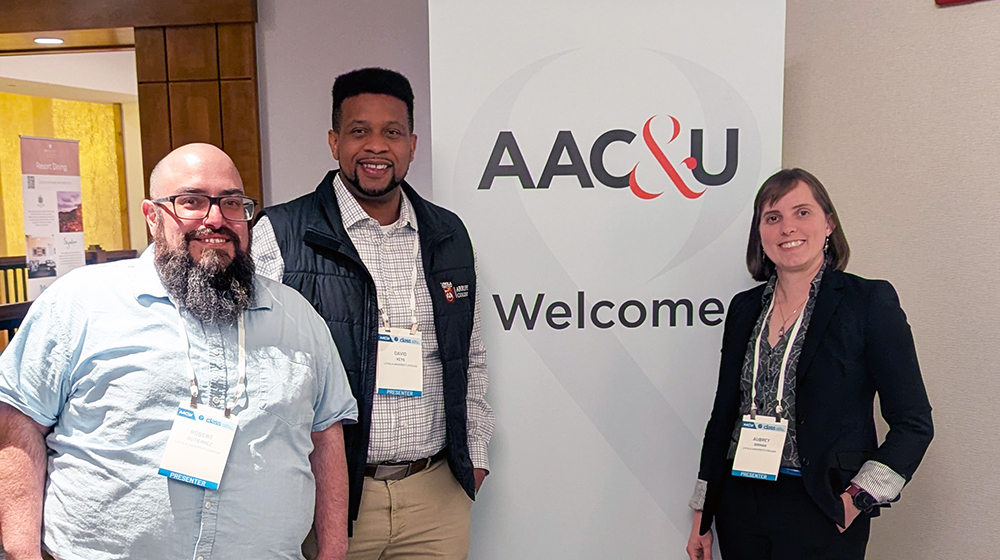 Three people posing at an AAC&U event beside a welcome sign, wearing conference badges